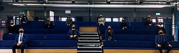 Students sit socially distanced on a blue raised seating bank while wearing masks.