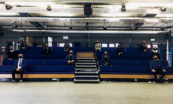Students sit socially distanced on a blue raised seating bank while wearing masks.