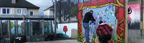 Two men stand on an outdoor stage while installing a colourful backdrop.