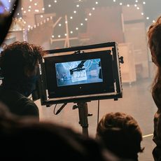 A group of people stand round a screen watching a dance production being filmed.