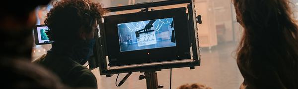 A group of people stand round a screen watching a dance production being filmed.