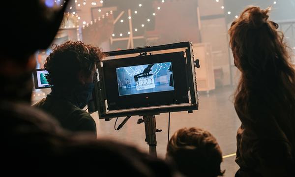A group of people stand round a screen watching a dance production being filmed.