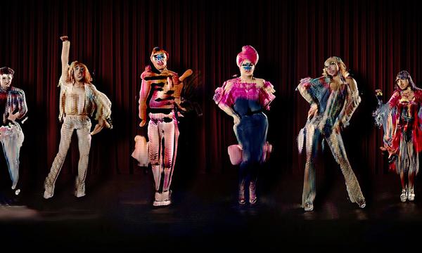 An image depicting The Zizi Show, a deepfake interactive drag cabaret. Six deepfake drag artists stand in a line in colourful costume while striking a variety of poses against a dark red curtain backdrop.