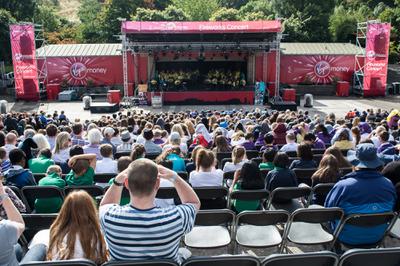 A crowd of children gather in Princes Street Gardens watching a youth orchestra play on a big red stage.