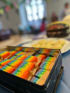 A tin of fudge coloured in rainbow stripes decorated with the letters LGBTQIA