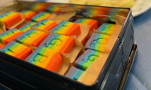 A tin of fudge coloured in rainbow stripes decorated with the letters LGBTQIA