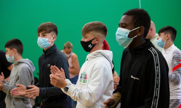 Boys wearing face coverings and hoodies clap their hands and follow along with a workshop