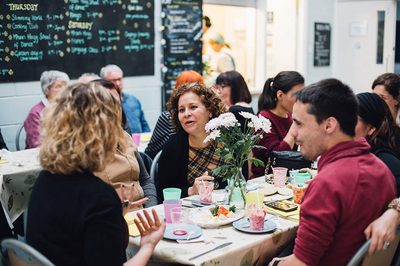 Group of people sat at a table talking with flowers in the middle and plates and cups on the table