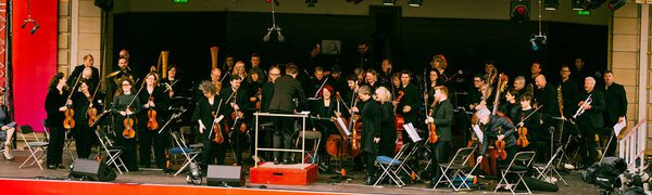 Orchestra on outside stage with red Virgin Money branding around the stage