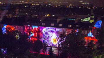 Looking over Edinburgh from rooftops with buildings in foreground covered with vibrant projections
