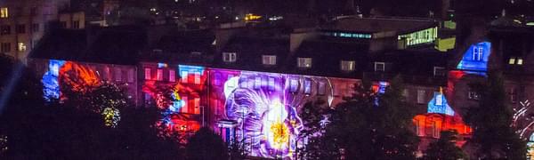 Looking over Edinburgh from rooftops with buildings in foreground covered with vibrant projections
