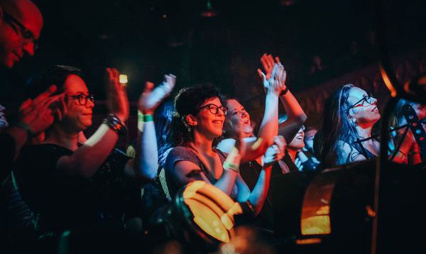 Group of people at a concert, standing, clapping, and smiling