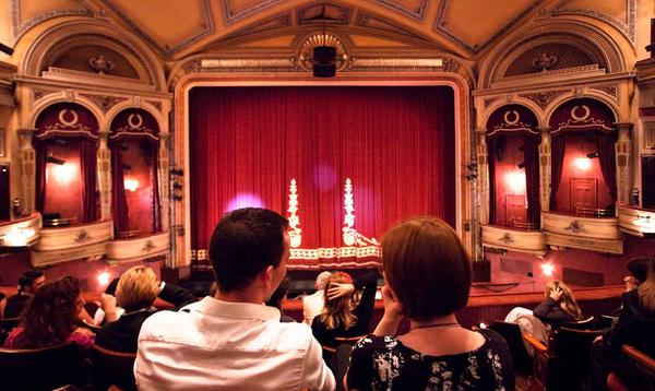 Couple sat in the dress circle of Edinburgh's Festival Theatre before a performance with the red curtain illumated