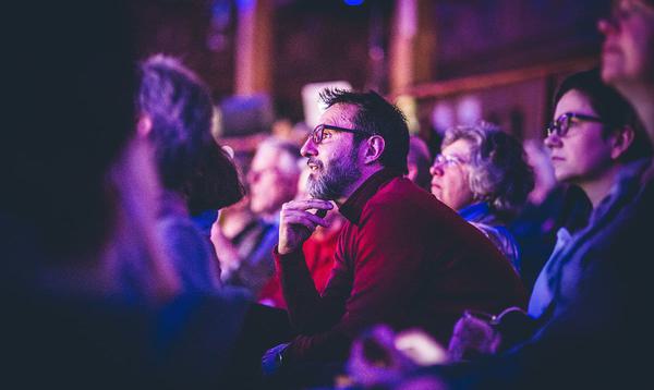 Audience focused on a man looking forward while sat in the audience of a presentation