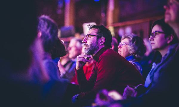 Audience focused on a man looking forward while sat in the audience of a presentation