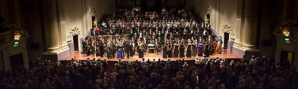 View looking down on audience with a large orchestra on a stage with singers in front in the background