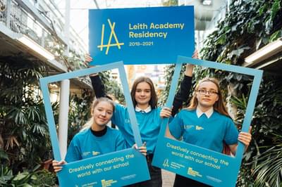 Three Leith Academy students in blue t-shirts holding boards and life-sized photo frames