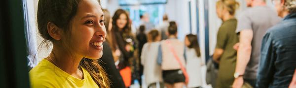 Girl in EIF branded yellow t-shirt smiling at a line of people walking out of focus away from the camera