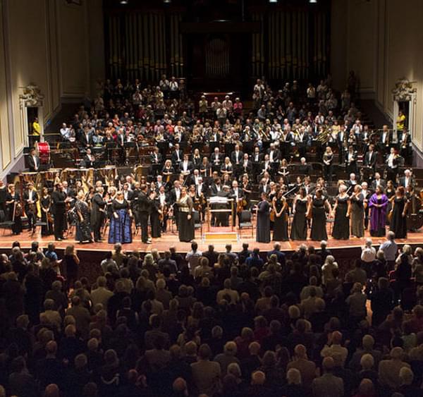 View looking down on audience with a large orchestra on a stage with singers in front in the background