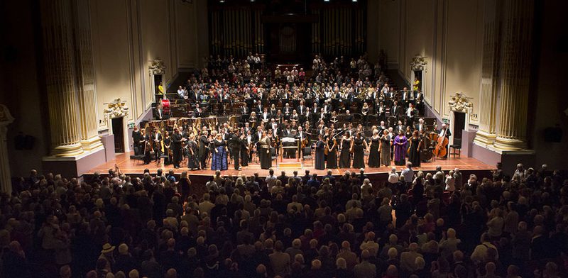 View looking down on audience with a large orchestra on a stage with singers in front in the background