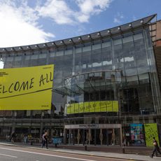 The glass exterior of Festival Theatre with Edinburgh International Festival branding plastered on it that reads 'Welcome All'