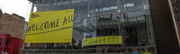 The glass exterior of Festival Theatre with Edinburgh International Festival branding plastered on it that reads 'Welcome All'