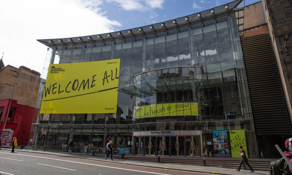 The glass exterior of Festival Theatre with Edinburgh International Festival branding plastered on it that reads 'Welcome All'