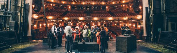 A view out across a theatre auditorium from a stage. A group of people gather on the stage during a Touch Tour.