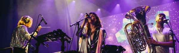 Artist and band on stage wearing silver with purple and yellow lights coming onto the stage