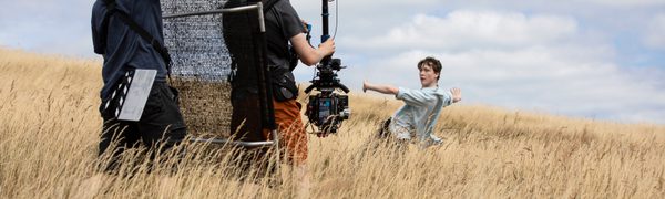 Two camera men stand in a field of corn filming a dancer in a blue shirt
