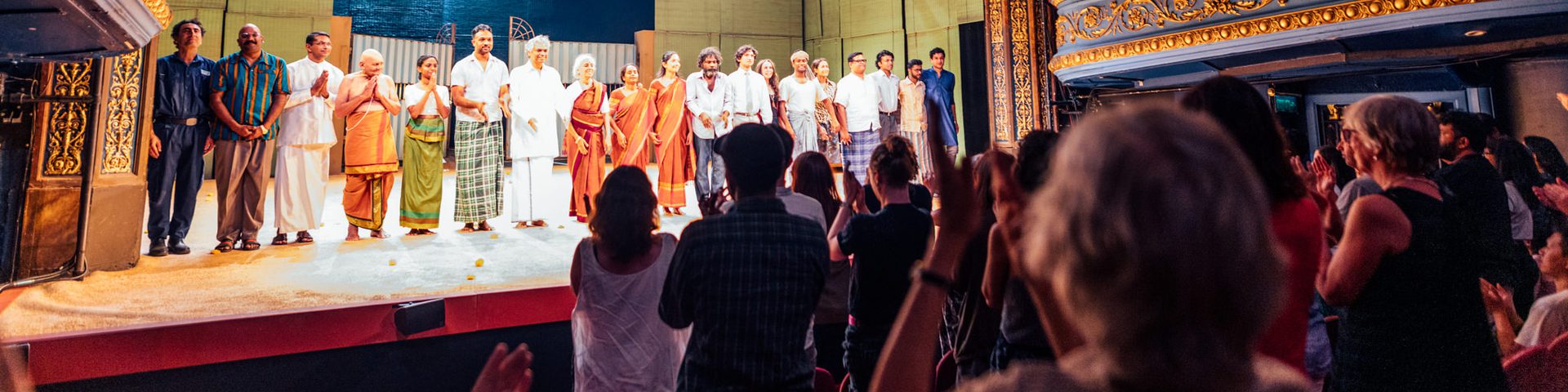 A group of performers in stand in a line on stage in front of a crowd giving a standing ovation