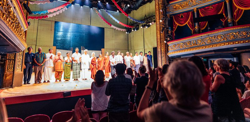 A group of performers in stand in a line on stage in front of a crowd giving a standing ovation