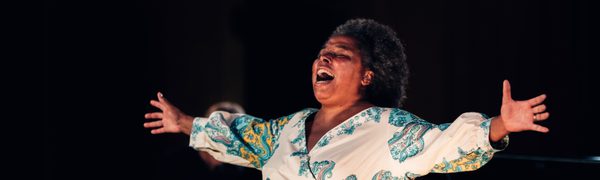 Andrea Baker performing onstage, singing with her arms outstretched.