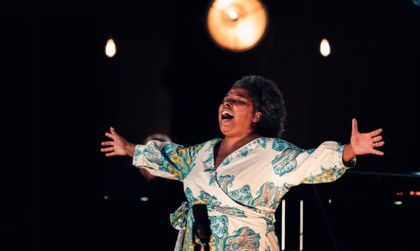 Andrea Baker performing onstage, singing with her arms outstretched.