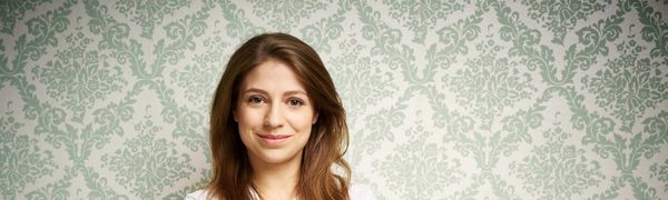 The conductor pictured wearing a white shirt, standing against green patterned wallpaper.
