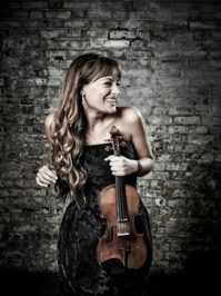 Nicola Benedetti looking to the left and smiling while holding her violin.