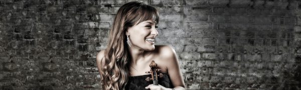 Nicola Benedetti looking to the left and smiling while holding her violin.