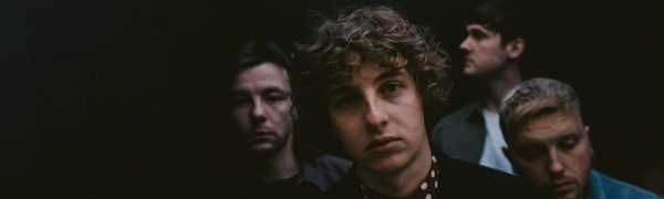 The Snuts pictured against a black backdrop, with the lead singer looking into the camera and the three other band members looking away.