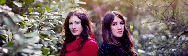 Rachel and Becky Unthank stand back to back in a forest