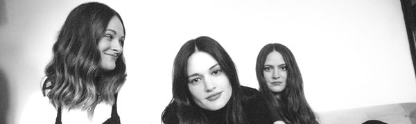 Black and white photo of the three sisters of The Staves, posing on a sofa