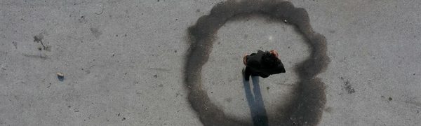 Aerial view of someone standing on grey sand, with a ring of dust around them.