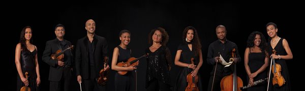 Members of the Chineke! Orchestra stand with their instruments, with Chi-chi Nwanoku standing in the middle