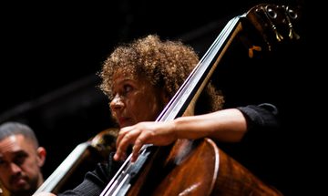 A close-up image of a member of the Chineke! Chamber Ensemble playing her cello, photographed from a low angle to show the position of her hand and bow.