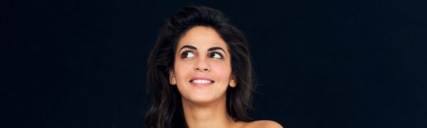 The singer pictured smiling while looking up and to the right, wearing a strapless dress and a silver pendant in the shape of Africa.