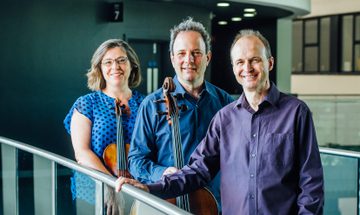 The three members of the Gould Piano Trio pictured on a balcony with cello and violin