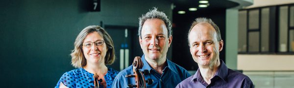 The three members of the Gould Piano Trio pictured on a balcony with cello and violin