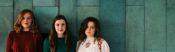 The three members of Sian stand in front of a green wall