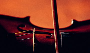 A close-up shot of a violin being played against a deep orange background