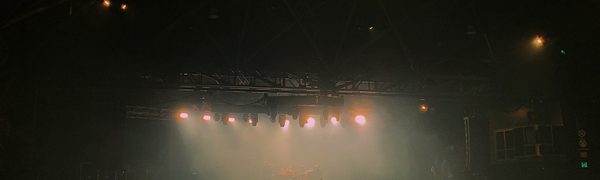 Silhouetted figures stand on stage with stage lights shining down in front of them.