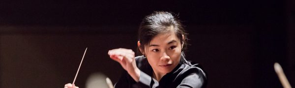The conductor pictured mid-movement, looking intently at the orchestra with her arms raised.